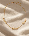Gold name necklace with three cursive names, Camila, Emma and Lucas, on linen