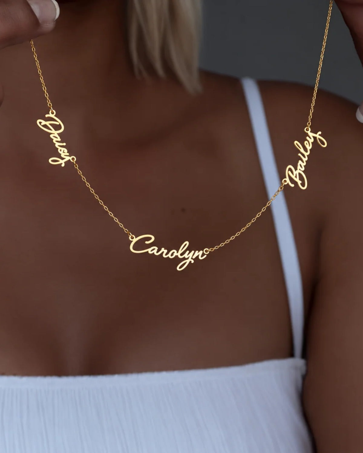 Necklace with the names Daisy, Carolyn and Bailey held up in cursive script